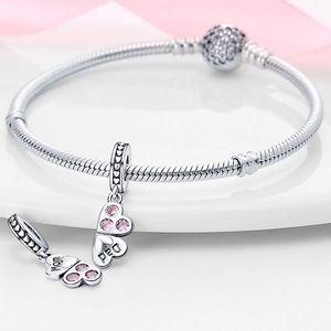Macro detail of silver charm bracelet with Mom and Dad heart charms on white ceramic tray