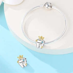 Close-up of silver tooth charms with golden crowns and sparkling pavé on a bangle