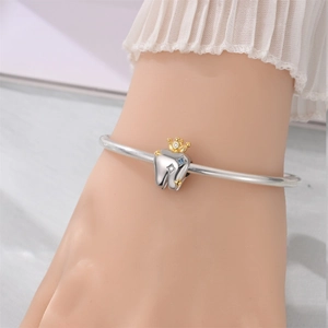 Macro detail of silver tooth charm with gold crown and colorful zircons on a bracelet
