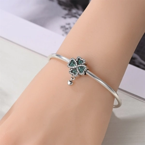 Macro view of silver-plated open bangle featuring a green clover and heart charm on wrist