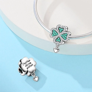 Macro detail of silver four-leaf clover charm with green stones and hope engraving