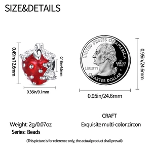 Detalle del dije fresa de esmalte rojo con circonitas junto a moneda para referencia de tamaño