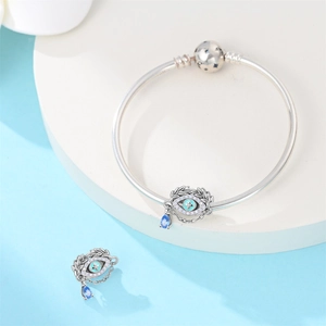 Close-up of silver charm bracelet with turquoise evil eye and blue teardrop pendant