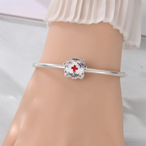 Close-up of a silver medical charm with a red cross on a metal beaded bracelet