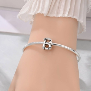 Close-up of polished silver bangle featuring a star-set crystal letter B charm pendant