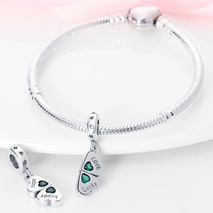 Nahaufnahme von silbernem Schlangenarmband mit grünen Herzanhängern und Glücksgravuren