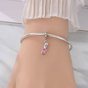 Detailed shot of a silver bangle with a pink bow bouquet charm on a model's wrist