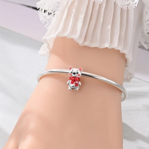 Primer plano de un dije de oso con bufanda roja en un brazalete de metal plateado