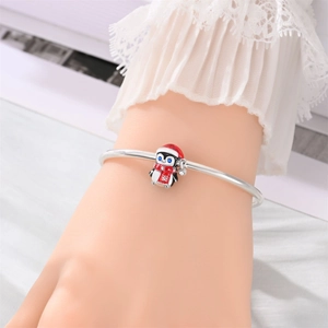 Detalle de brazalete plateado con dije de pingüino con gorro de Navidad y bufanda roja festiva