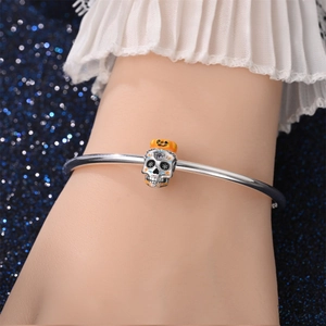 Detail van een zilveren Halloween-armband met bedeltjes van een schedel en oranje pompoen