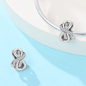 Silver infinity charm with cubic zirconia pavé on a matching bracelet on blue display