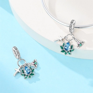 Macro detail of silver lotus charm with blue gemstone and cross pendant on a bracelet