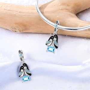 Vista detallada del charm de pingüino plateado con gema azul sobre fondo de seda invernal