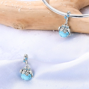 Detail eines blauen Glasanhängers mit silbernen Wellen auf weißem Seidenhintergrund