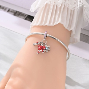 Detalle de pulsera de plata con dije 'smile', oso con suéter rojo y un copo de nieve azulado
