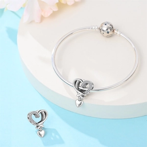 Detail of silver heart charms and bangle with blue star engraved clasp on white stand