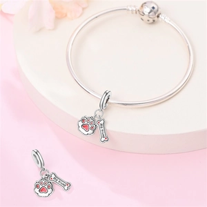 Dettaglio macro dello charm in argento con zampa rossa e osso con incisione per bracciali