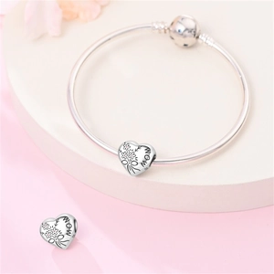 Dettaglio macro del charm a cuore in argento S925 con incisione MOM e fiori