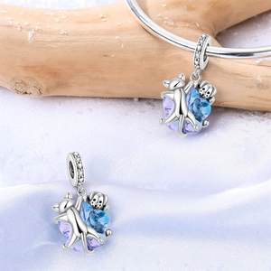 Detalle de dijes de plata de gato y perro abrazando un cristal degradado azul-violeta