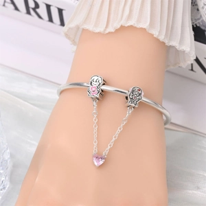 Detail of silver bangle featuring boy and girl charms with a pink heart crystal link