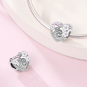 Macro detail of heart charm with pink enamel flowers and zircons on silver bracelet