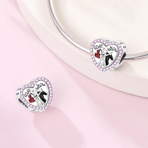 Macro detail of silver heart charm with pink zircons and dancing couple engraving
