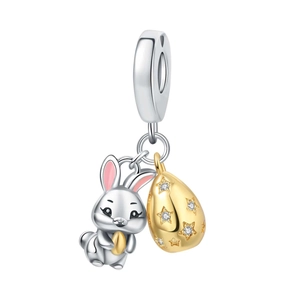 Détail d'un charm lapin en argent tenant un œuf doré à motifs d'étoiles et émail rose