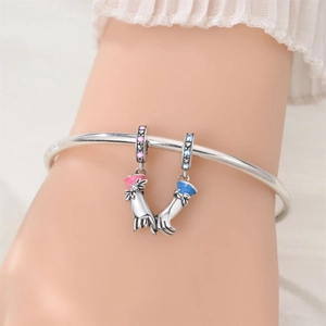 Detailed view of silver charm bracelet with pink and blue hand-holding heart pendants