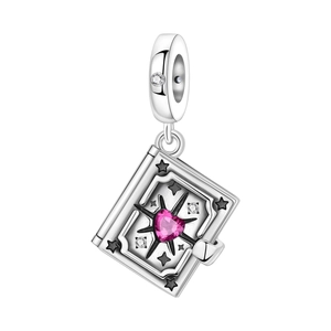Macro detail of silver book charm with pink heart gemstone and starry engravings