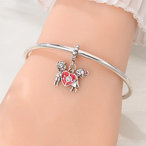 Close-up of silver-plated heart charm with boy and girl figures on a bangle bracelet
