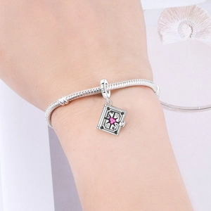 Detail of silver snake chain bracelet with star and pink heart stone book charm
