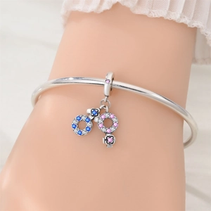 Close-up of a silver bangle featuring a double-ring pendant with blue and pink pavé crystals