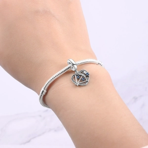 Makro-Detail eines silbernen Herz-Kronen-Anhängers mit blauen Kristallen auf Schlangenarmband