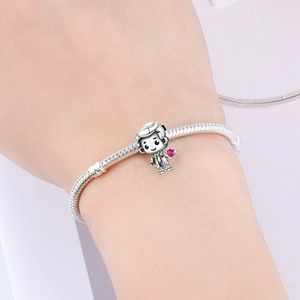 Detail of silver snake chain bracelet featuring a cartoon boy charm with a pink heart stone
