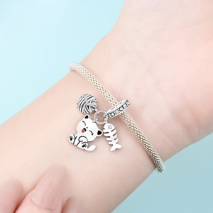 Pulsera plateada con dijes de gato, ovillo de lana y espina de pescado en la muñeca