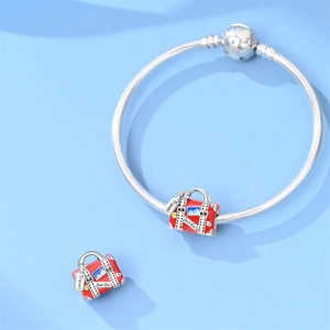 Detail of a red travel suitcase charm with Just Go engraving on a silver snake chain bracelet