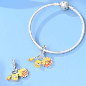 Detail of silver snake chain bracelet with brush, handbag, and daisy charms on blue background