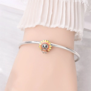 Close-up of a silver charm bracelet with a cute yellow sunflower pendant on a wrist