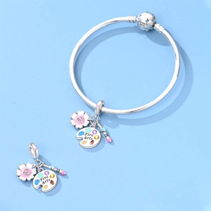 Close-up of silver travel charms featuring pink enamel flowers and an artist palette pendant
