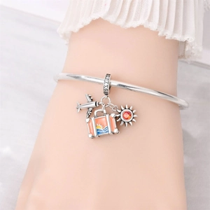 Close-up of travel themed charms including airplane and orange suitcase on a silver bangle