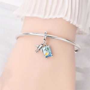 Close-up of travel charm bracelet with silver airplane and blue enamel suitcase detail