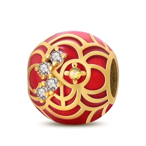 Dettaglio macro dello charm in smalto rosso con motivi dorati e zirconi brillanti