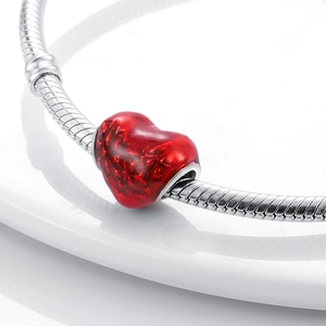 Close-up of a red marble-textured heart charm on a silver snake chain bracelet