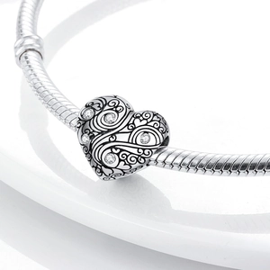 Macro shot of silver heart charm with scroll textures and zircons on snake chain