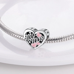 Detailed macro view of heart charm with 'mi amor' text and pink enamel hearts on a bracelet