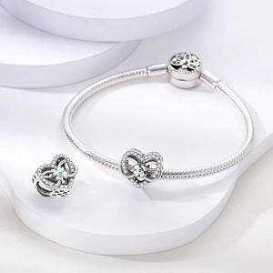 Macro shot of silver snake chain bracelet and hollow heart charms with green gems