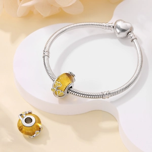 Macro shot of silver snake chain bracelet with yellow glass charm and ginkgo leaf pattern