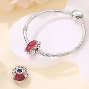 Detail of silver snake chain bracelet with heart clasp and two red floral glass beads