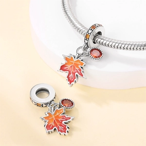 Macro shot of a silver squirrel charm and orange enamel maple leaf with red zircon gems