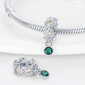 Macro detail of silver daisy charm with yellow zircon and emerald green gemstone pendant